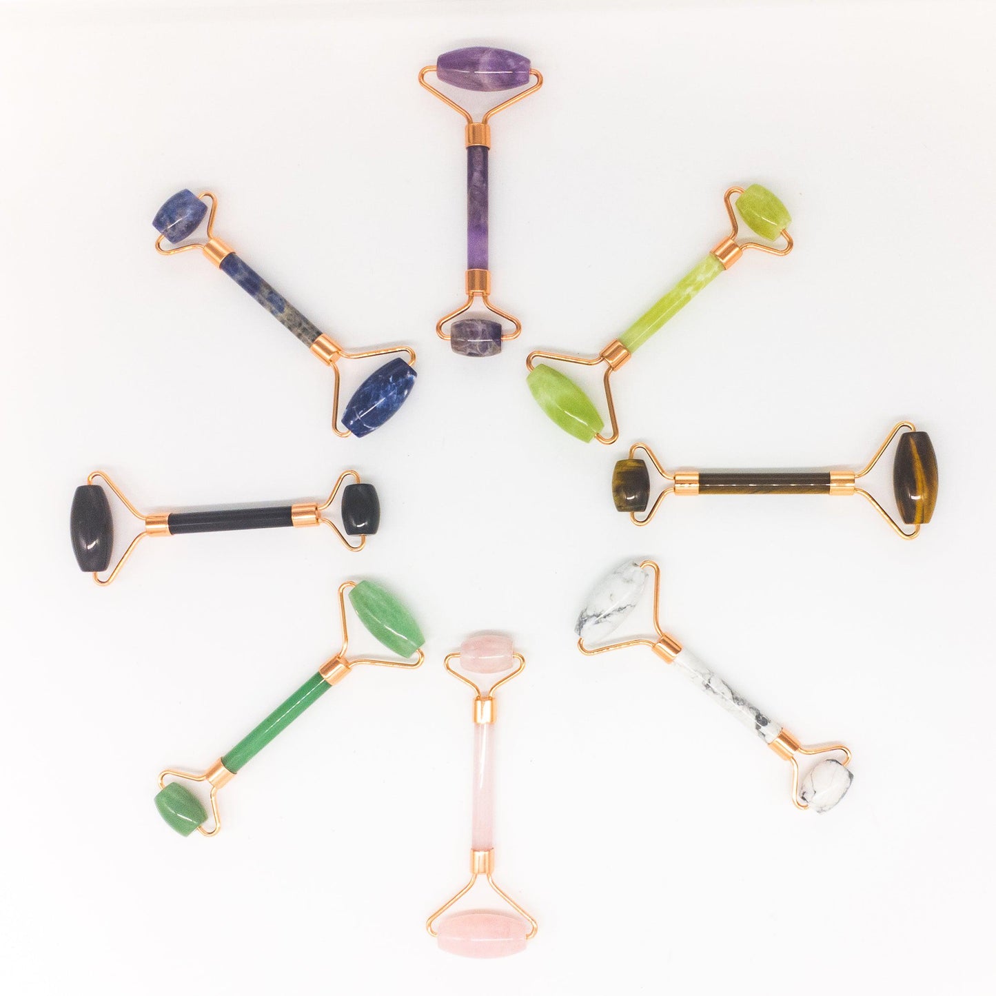 A collection of face rollers made with various gemstones and copper-infused metal, displayed against a white background.